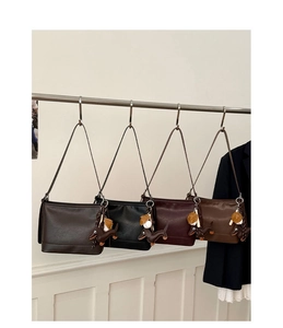 Reihe von Leder-Beuteltaschen mit Dackel-Anhänger an Haken vor minimalistischem Hintergrund