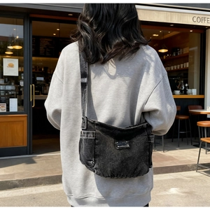 Detail showing the vintage black washed denim texture and side pocket of the shoulder bag