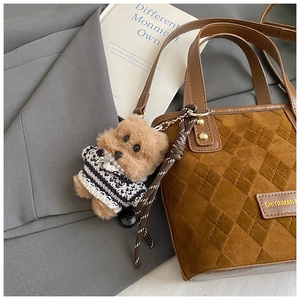 Close-up of plush puppy bag charm in striped sweater on brown quilted bucket bag