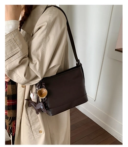 Details einer dunkelbraunen Leder-Beuteltasche mit Anhängern, getragen von einem Model