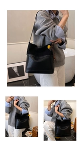 Detail of black bucket bag featuring matte leather texture and yellow pompom tassel