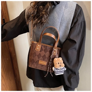 Detail showing vintage brown quilted crossbody bucket bag with cute bear charm on model