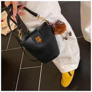 Detail of black leather bucket bag with retro gold buckle and cute plush charm pendant