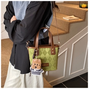 Close-up of matte green bucket bag with diamond lattice pattern and cute bear pendant