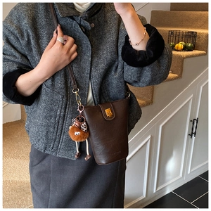 Detail of dark brown leather bucket bag featuring gold hardware and leopard bow plush charm