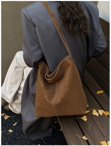 Detail view of large brown hobo bag with white stitching on a wooden bench