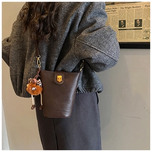 Detail of dark brown leather bucket bag with leopard print charm on a grey wool coat