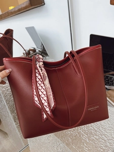 Chic burgundy tote bag with silk scarf on handle and office accessories background
