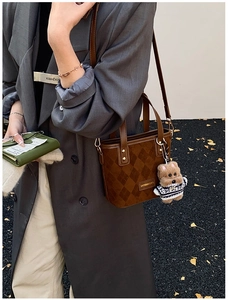 Detail of dark brown checkered bucket bag with leather texture and plush bear charm