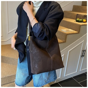 Detail of dark brown suede tote bag with white contrast stitching and gold metal buckle
