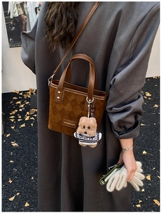 Close-up of brown suede bucket bag with checkered texture and plush dog pendant