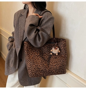 Detailed view of the leopard print tote bag featuring brown leather straps and plush charm