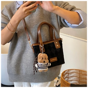 Close-up of black quilted bucket bag with a brown handle and a cute teddy bear charm