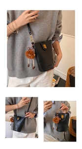 Detail of black mini bucket bag with gold clasp and cute brown plush doll charm pendant