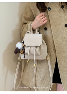Dettaglio zaino in pelle beige con ciondoli a nappa e orecchie di peluche su cappotto beige