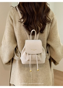 Dettaglio dello zaino minimalista in pelle crema con coulisse a sfere dorate e logo