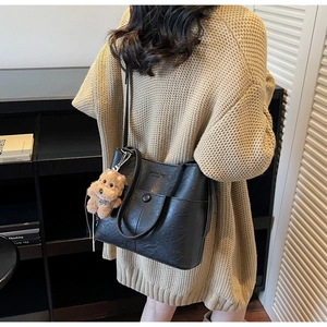 Detail of black faux leather tote bag with a cute brown plush dog charm on shoulder