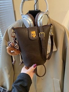 Brown vintage leather bucket bag with gold hardware and plush charm held against a trench coat