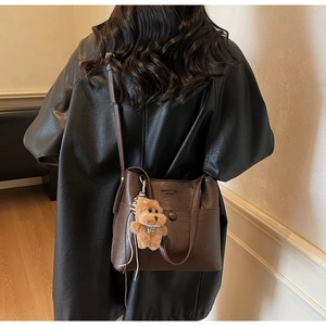 Detail of dark brown leather shoulder bag with vintage engraving and plush bear charm