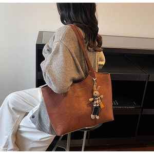 Detail of a brown leather tote bag with a plaid bunny charm and gold logo on a model