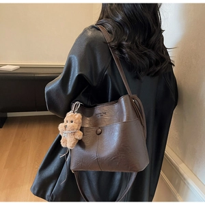 Detail of dark coffee leather bucket bag with embossed logo and plush bear charm accessory