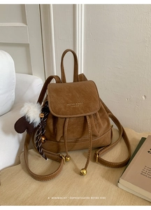 Dettaglio dello zaino vintage in pelle scamosciata marrone con cuciture bianche e ciondolo