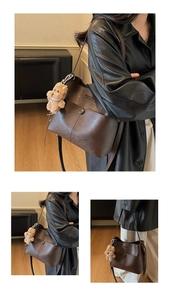 Detail of vintage brown leather tote bag with logo embossing and cute plush bear charm