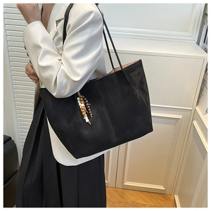 Detail of black suede tote bag with decorative bead tassels and long leather shoulder straps