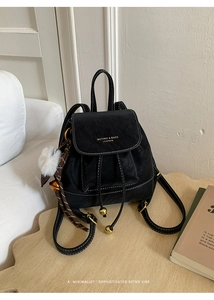 Dettaglio dello zaino vintage in pelle nera con cuciture bianche e ciondolo a pompon