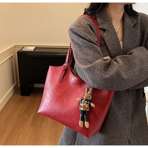 Detail of red leather tote bag with rabbit charm worn with grey blazer