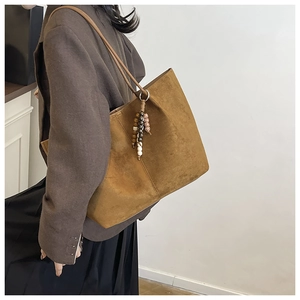 Detail of a brown suede tote bag with ethnic wooden bead charm worn by a model
