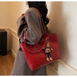Detail of red vintage tote bag with oil-wax texture and cute rabbit charm on shoulder strap