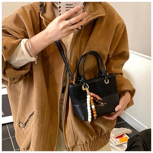 Detail of black crossbody bucket bag with colorful bead tassel and golden D-ring accent