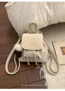 Dettaglio mini zaino in pelle crema con logo dorato e ciondolo a pompon in peluche morbido
