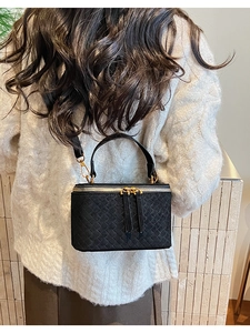 Detail of a black woven leather mini box bag worn by a model in a cozy white sweater