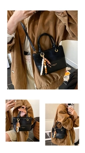 Detail of black leather bucket bag with wooden bead charm and crossbody strap