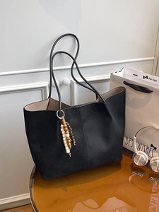 Minimalist black matte tote bag with rustic wooden bead tassel on a brown table