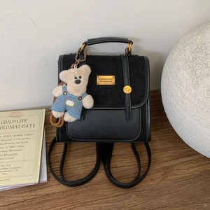 Close-up of black retro leather backpack with golden metal plate and plush bear charm