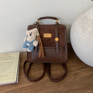 Detail of vintage suede and leather backpack with a plush bear charm and gold plaque