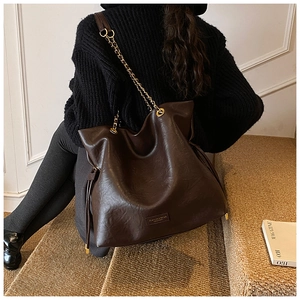 Detail of dark brown textured leather tote with gold chain strap and side drawstring
