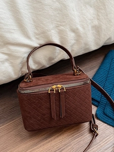Brown woven box bag with top handle and adjustable shoulder strap on a cozy background