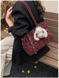 Detalle del bolso tote burdeos de cuero mate con ojales metálicos y colgante de conejo