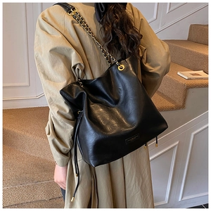 Detail of black pebbled leather tote bag with elegant chain strap and side drawstrings