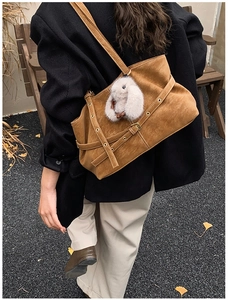 Brown suede tote bag with decorative belts and white plush rabbit charm in autumn setting