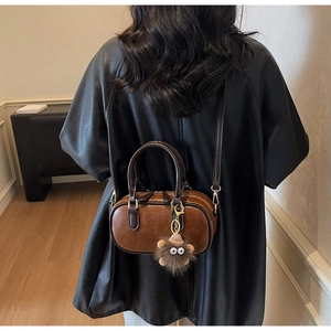 Detail of dark brown cylindrical bag with furry monster eye charm worn cross-body