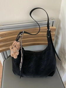 Grand sac hobo noir mat avec pendentif ours en peluche et glands en cuir sur une chaise