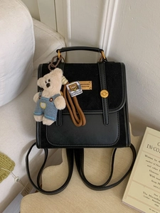 Minimalist black leather and suede backpack with a cute bear charm on a wooden table