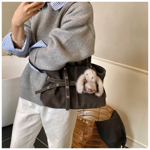 Close-up of vintage brown tote bag with decorative metal eyelets and a plush rabbit charm
