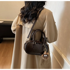 Detail der braunen Vintage-Handtasche mit Plüschanhänger kombiniert mit einem Trenchcoat