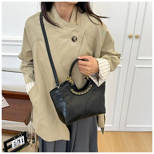 Dettaglio borsa a secchiello nera con catena dorata abbinata a un trench beige moda